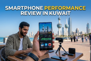 The screen displays a clear performance test graph with high scores, confirming a rigorous Smartphone Performance Review in Kuwait. In the background, a content creator sits at a tech-laden table against the iconic backdrop of the Kuwait City skyline. A small camera on a mini-tripod is set up for filming, suggesting a review being recorded on location. The overall atmosphere emphasizes mobile technology testing and creation